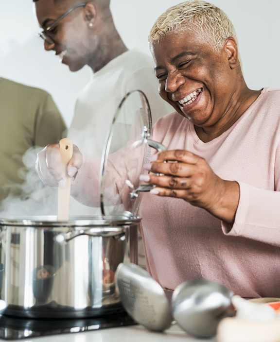 A group of people are gathered around a kitchen counter, cooking and laughing together.