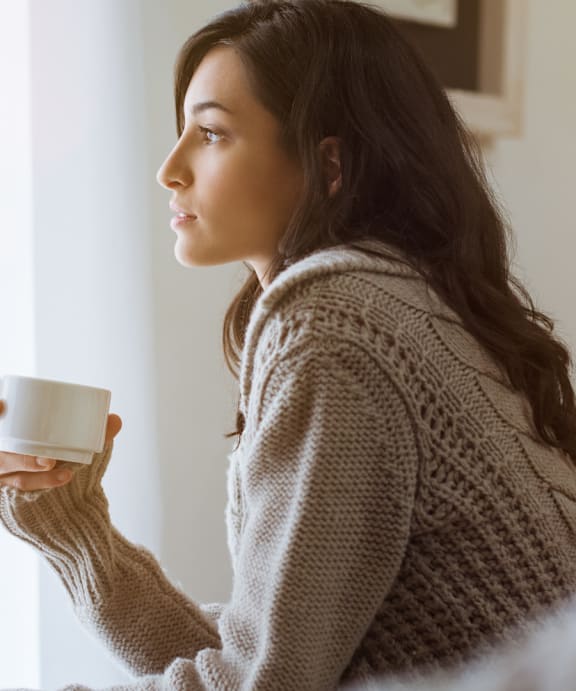 A woman in a sweater is holding a cup.