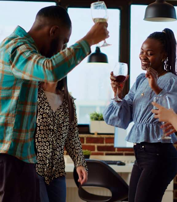 Three people toasting with drinks in a room with a brick wall.