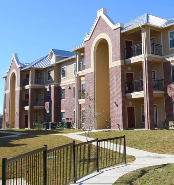 A large apartment complex with a black fence in front.