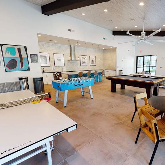 Roosevelt Row Resident Lounge The common room at Roosevelt Row, with a table tennis table, foosball table, a pool table, a TV, a bar counter with bar stools, and a table and chairs.
