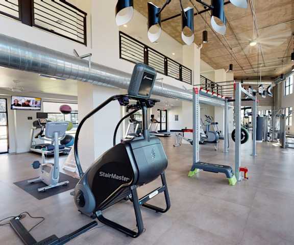Roosevelt Row Fitness Center A spacious gym with cardio machines, windows, TVs, and weights at Roosevelt Row Apartment Homes.