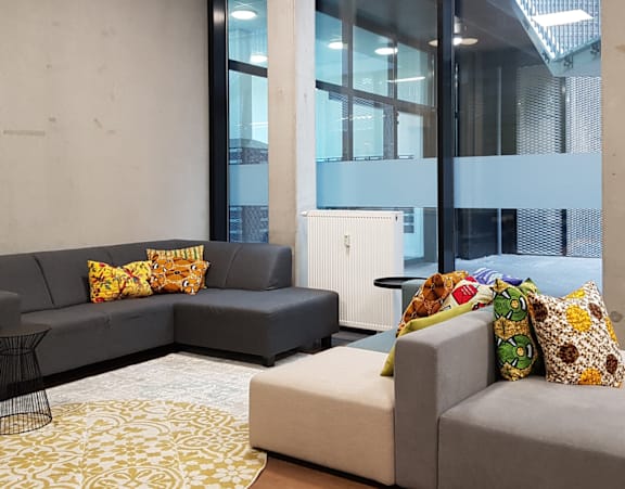 A grey couch with yellow pillows sits in a room with a large window.