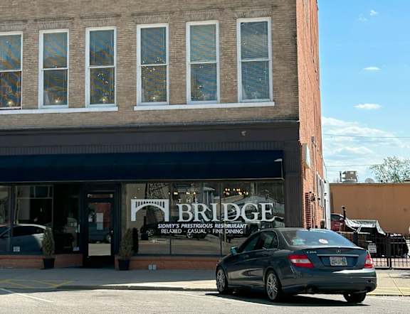 A car is parked in front of a store called Bridge.