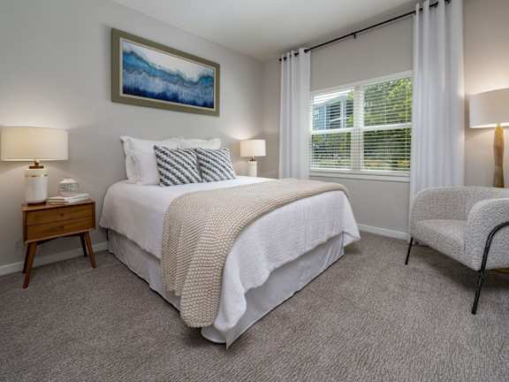 A bedroom with a large bed, a chair, and a painting on the wall.