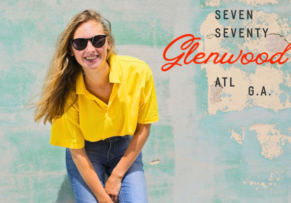 a woman wearing a yellow shirt and jeans against a blue wall