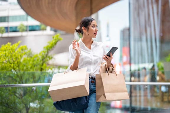 a woman holding shopping bags looking at her cell phone
