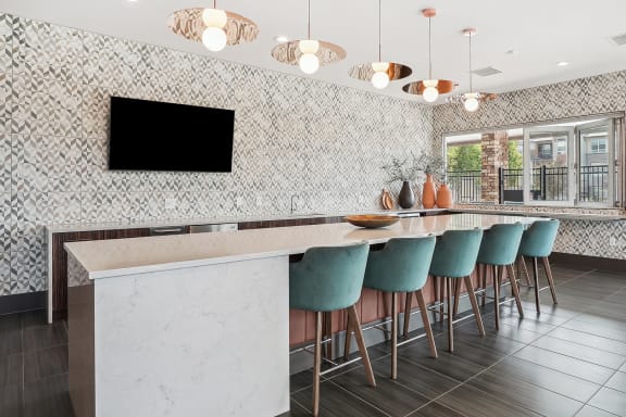 a kitchen with a long bar with blue chairs and a television