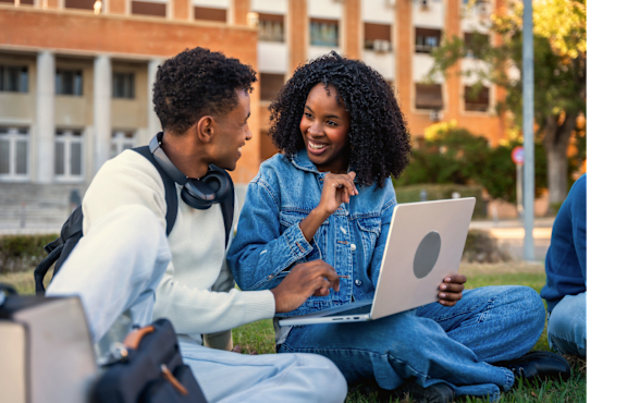 Two people sitting on the grass with a laptop.