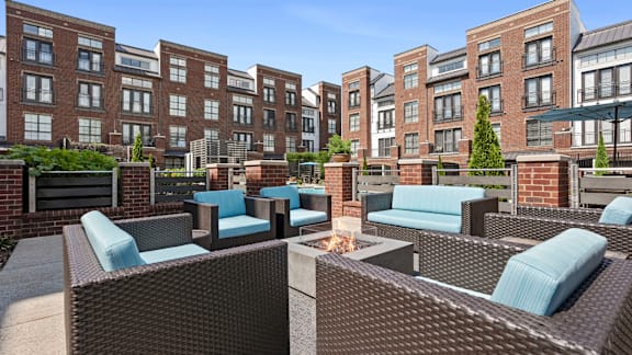 A patio with blue cushioned furniture and a fire pit in front of a brick building.