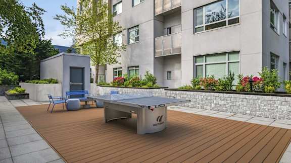 A ping pong table is on a wooden deck in front of a building.