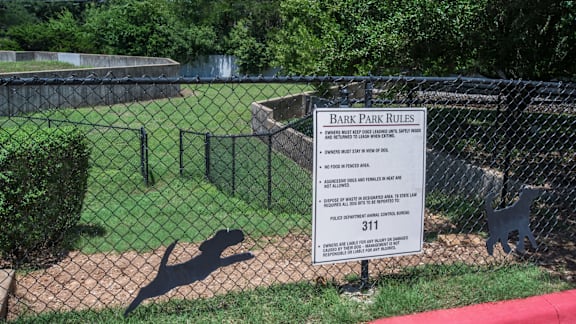 A sign in front of a fence that says Bark Park Rules.