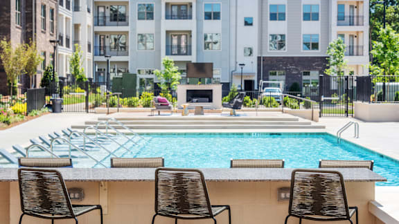 A pool surrounded by chairs and a building in the background.
