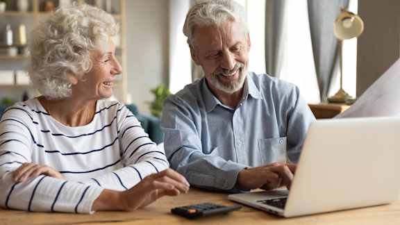 a man and woman sitting at a table looking at a laptop computer