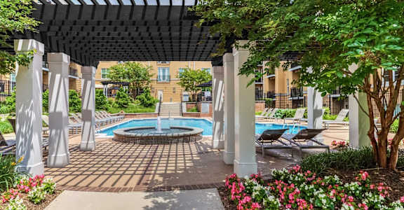 A pool area with a pergola and chairs.