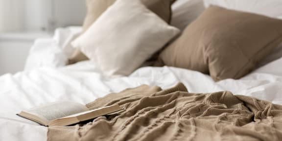 A book lies open on a bed with white sheets and pillows.