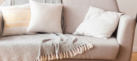A grey couch with a white pillow and a beige throw blanket.