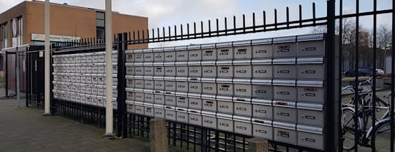 A row of mailboxes are lined up on a black fence.