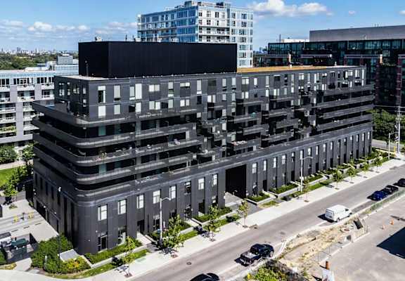 A large black building with many windows is surrounded by other buildings and a parking lot.