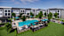 A large swimming pool surrounded by a fence and chairs is in the foreground of a residential area.