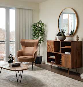 A living room with a brown chair, a round mirror, and a wooden shelf.