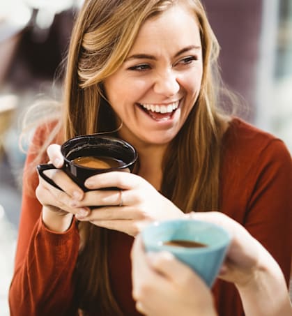two women sitting at a table laughing and drinking coffee