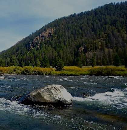 A river flows through a valley with a large rock in the foreground.
