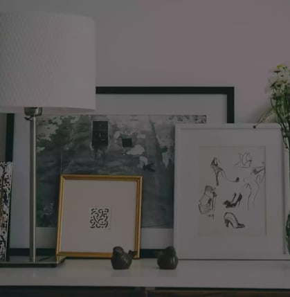 A collection of framed art pieces and a vase with flowers are displayed on a shelf.