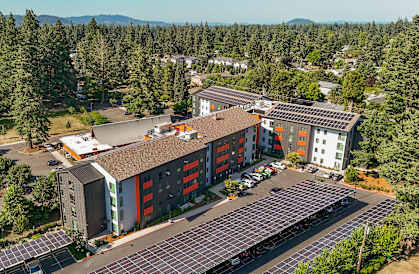 A modern building with solar panels on the roof is surrounded by trees.