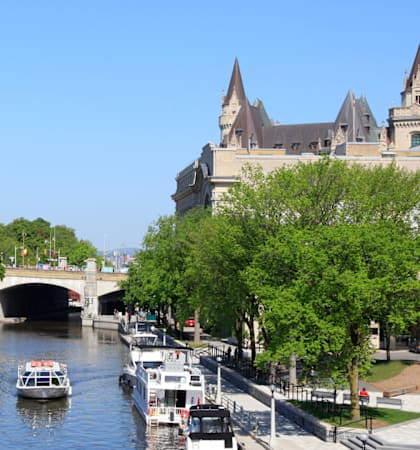 A boat is sailing under a bridge in a canal with a castle in the background.