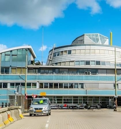 A modern building with a curved glass facade and a yellow stripe on the top.