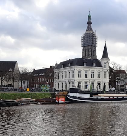 A church with a tall steeple stands in the middle of a town by the water.