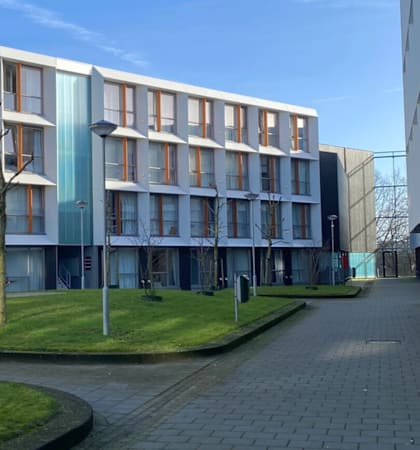 A modern building with a glass facade and a green lawn in front.