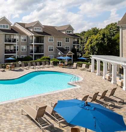 a swimming pool with chairs and umbrellas in front of an apartment building
