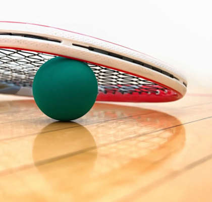 A green ball is on the ground next to a tennis racket.