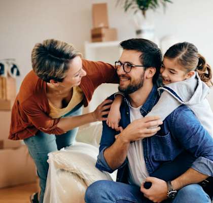 A family of three is sitting on a couch surrounded by moving boxes.