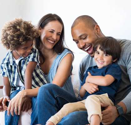 A family of four is sitting on a couch together.