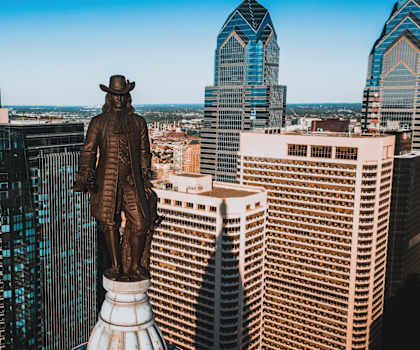 A statue of a man stands in front of a city skyline.