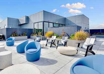 A modern building with blue chairs and tables in front.