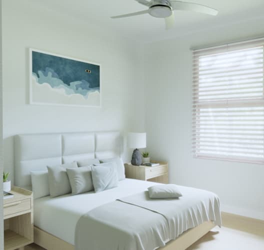 A bedroom with a bed, a ceiling fan, a nightstand with a lamp, a potted plant, and a painting on the wall.