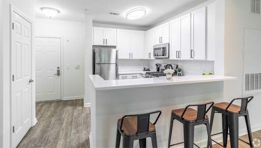 a kitchen with white cabinets and a counter with three stools