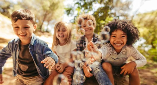 Four children are playing with bubbles in a sunny outdoor setting.