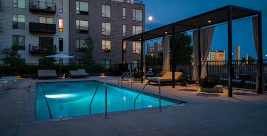 a pool is lit up at night in front of an apartment building