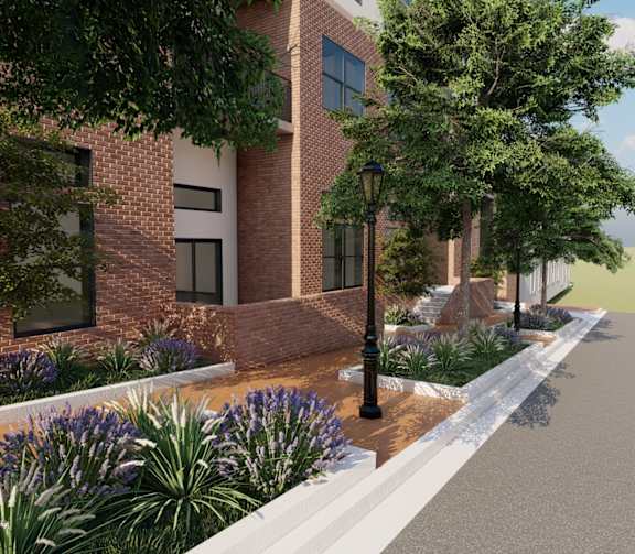 A street view of a building with a brick facade and a sidewalk lined with plants and a lamp post.