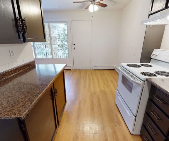 An empty kitchen with white appliances and granite counter tops at Broadmoor Apartments. 