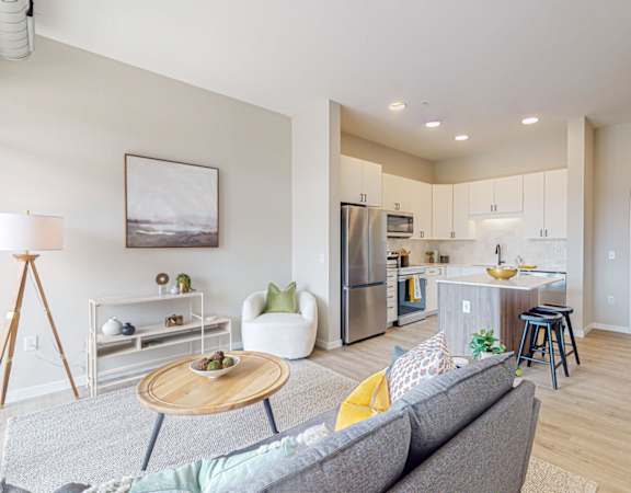 a living area with a couch coffee table and a kitchen in the background