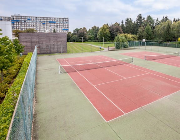 A tennis court with red and green markings surrounded by a fence.