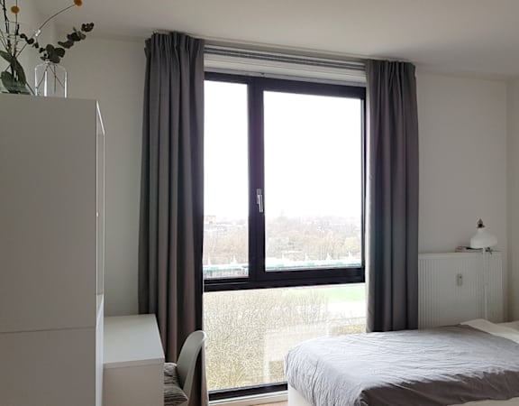 A bedroom with a large bed and a window with curtains.