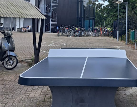 A grey table tennis table in the middle of a brick courtyard.