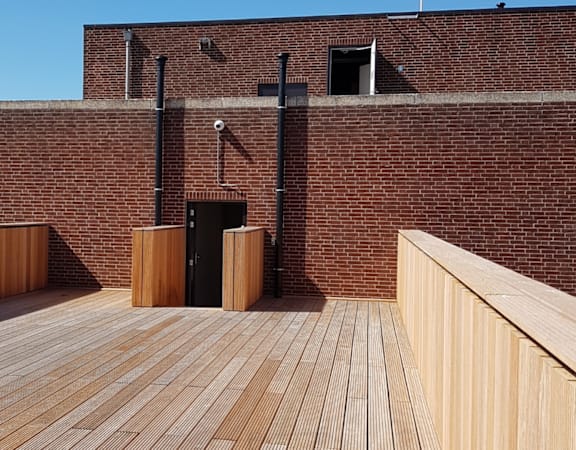 A wooden deck with a brick wall and a black door.